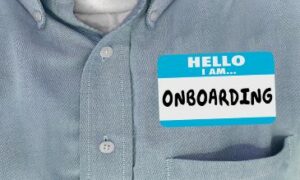 A person is wearing an adhesive nametag that reads "Hello, I am Onboarding" on their blue button-down shirt.