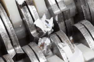 Close up image of small bits of paper between blades of an industrial paper shredder